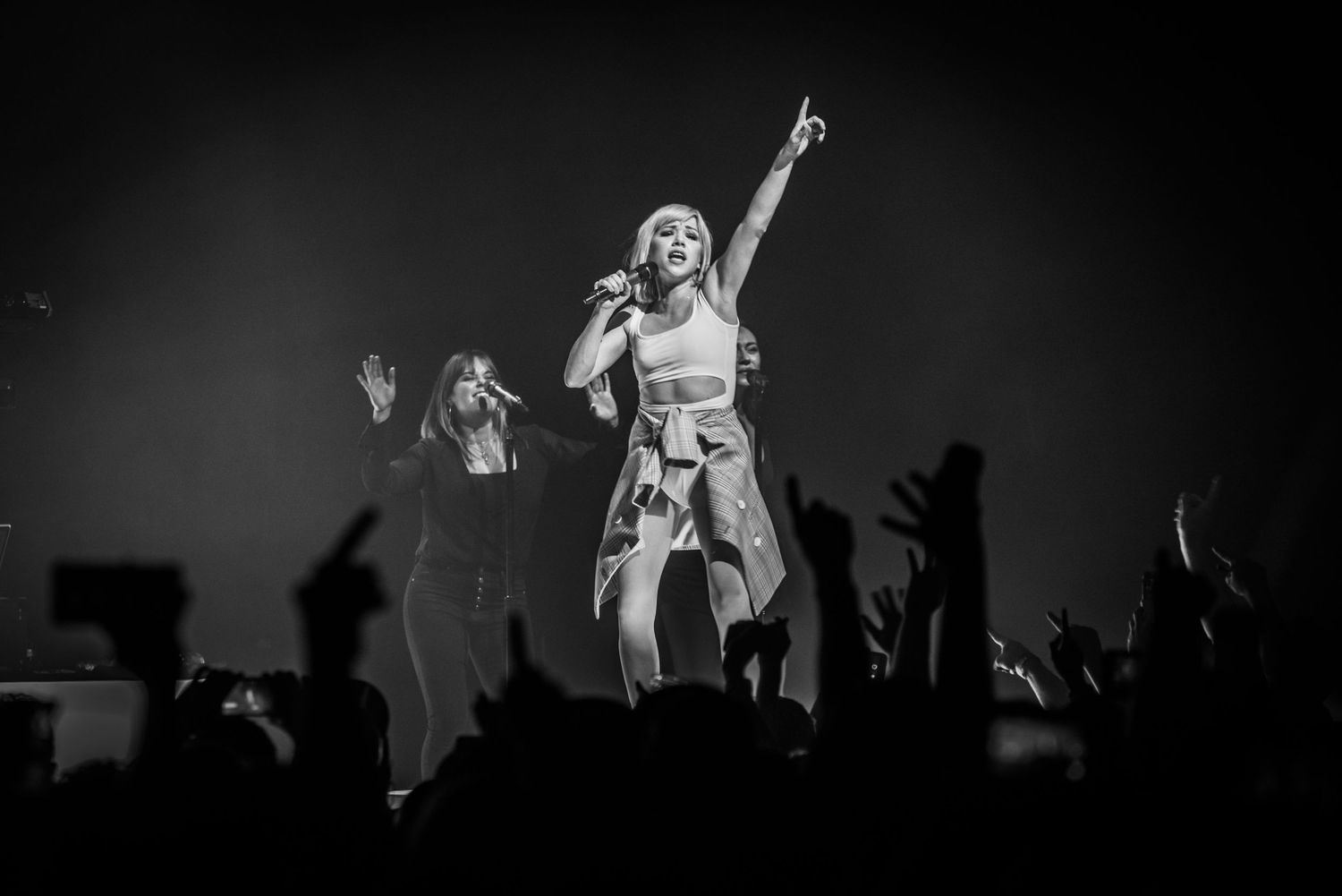 Black and white concert photo showing energetic performance with crowd silhouettes.