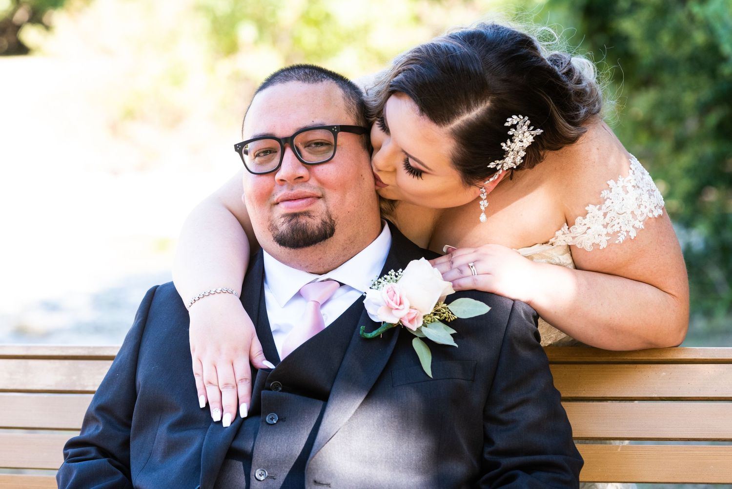 Romantic wedding portrait of couple sharing an intimate moment on wooden bench outdoors.