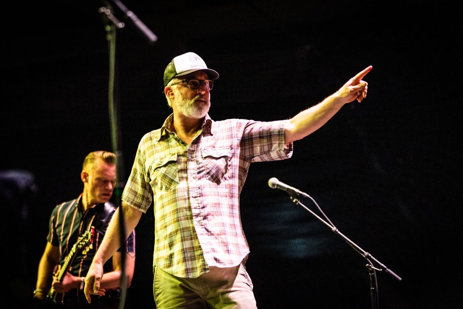 A performer in a baseball cap points while singing on stage during a concert performance.
