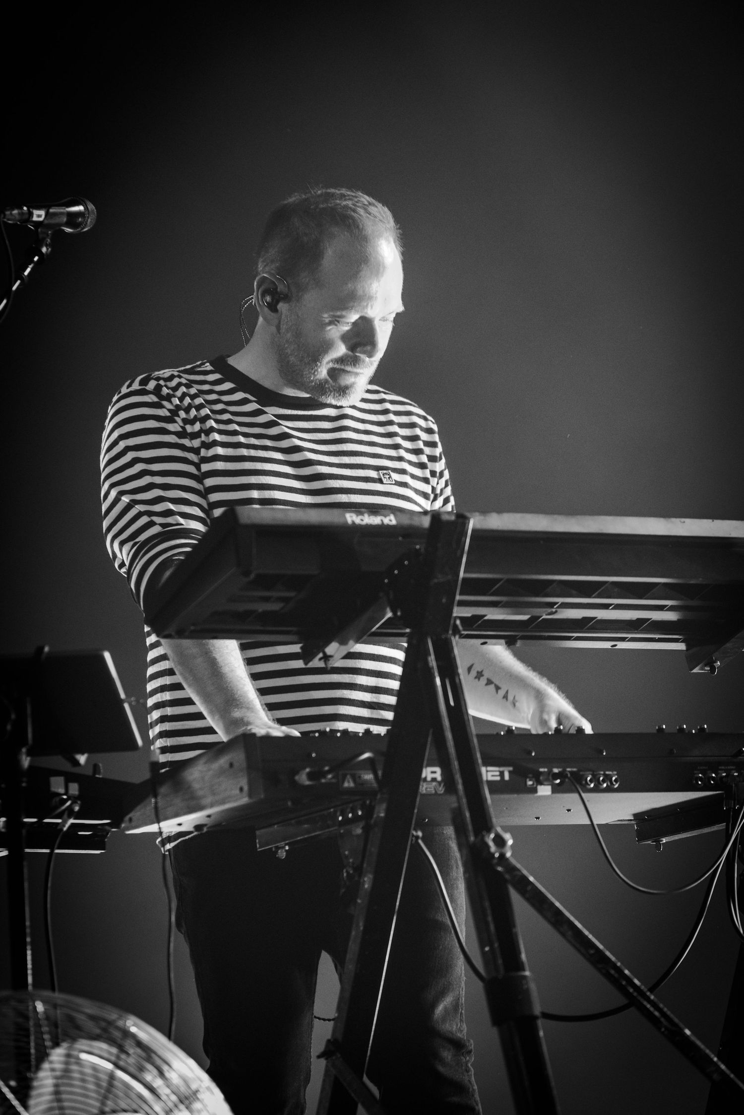 Musician in striped shirt plays keyboard during dramatic stage performance.