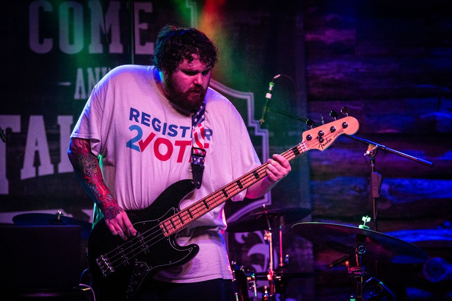 Bass guitarist in Register To Vote shirt performing under colorful stage lights.
