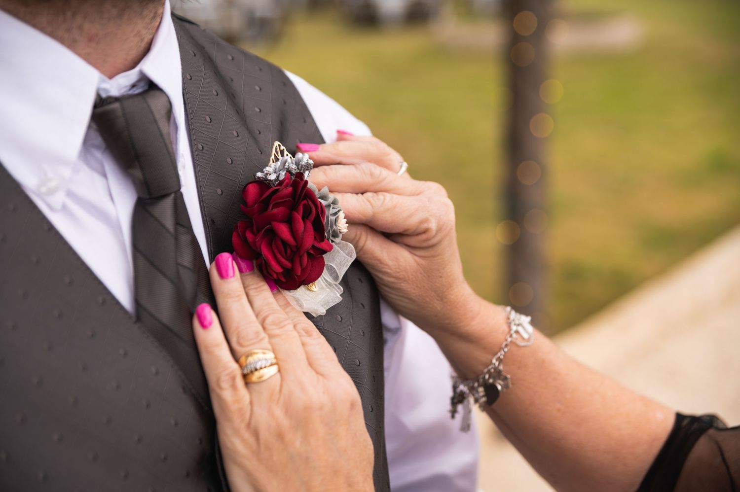 Hands arranging deep red rose boutonniere on grey suit vest.