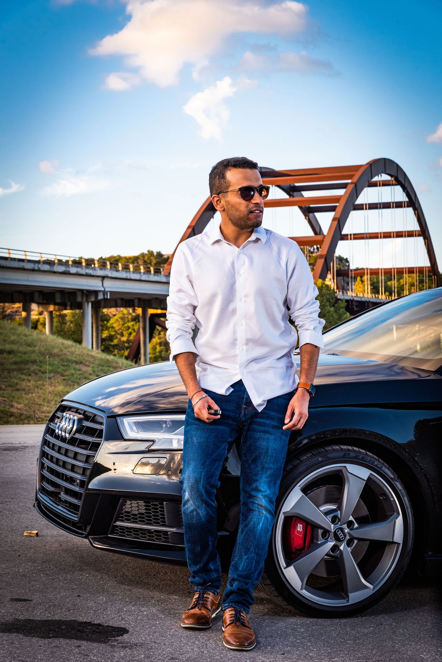 Black Audi sedan showcased near rustic bridge architecture with blue skies and scenic backdrop.