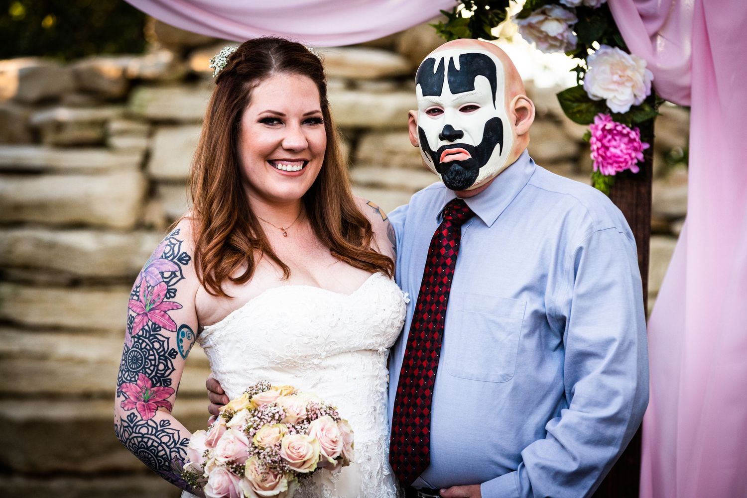 Bride in white lace dress with guest in unique face paint at outdoor wedding.