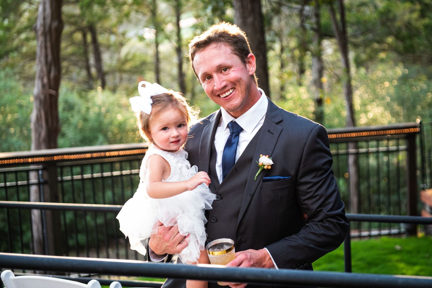 A tender moment between formal-dressed pair and small child in white dress on outdoor deck.