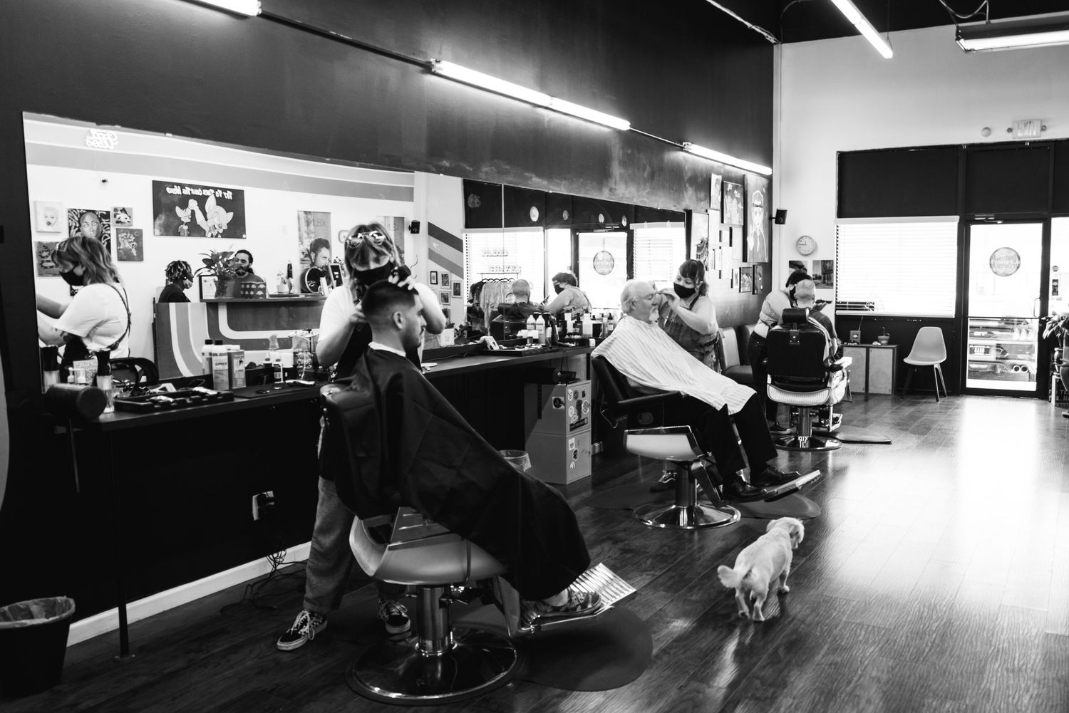 Black and white image of a busy barbershop interior with stylists working.