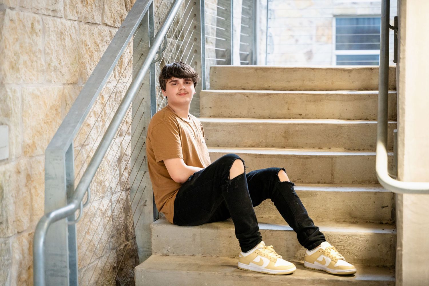 Someone in brown shirt and black jeans relaxes on outdoor stairs.