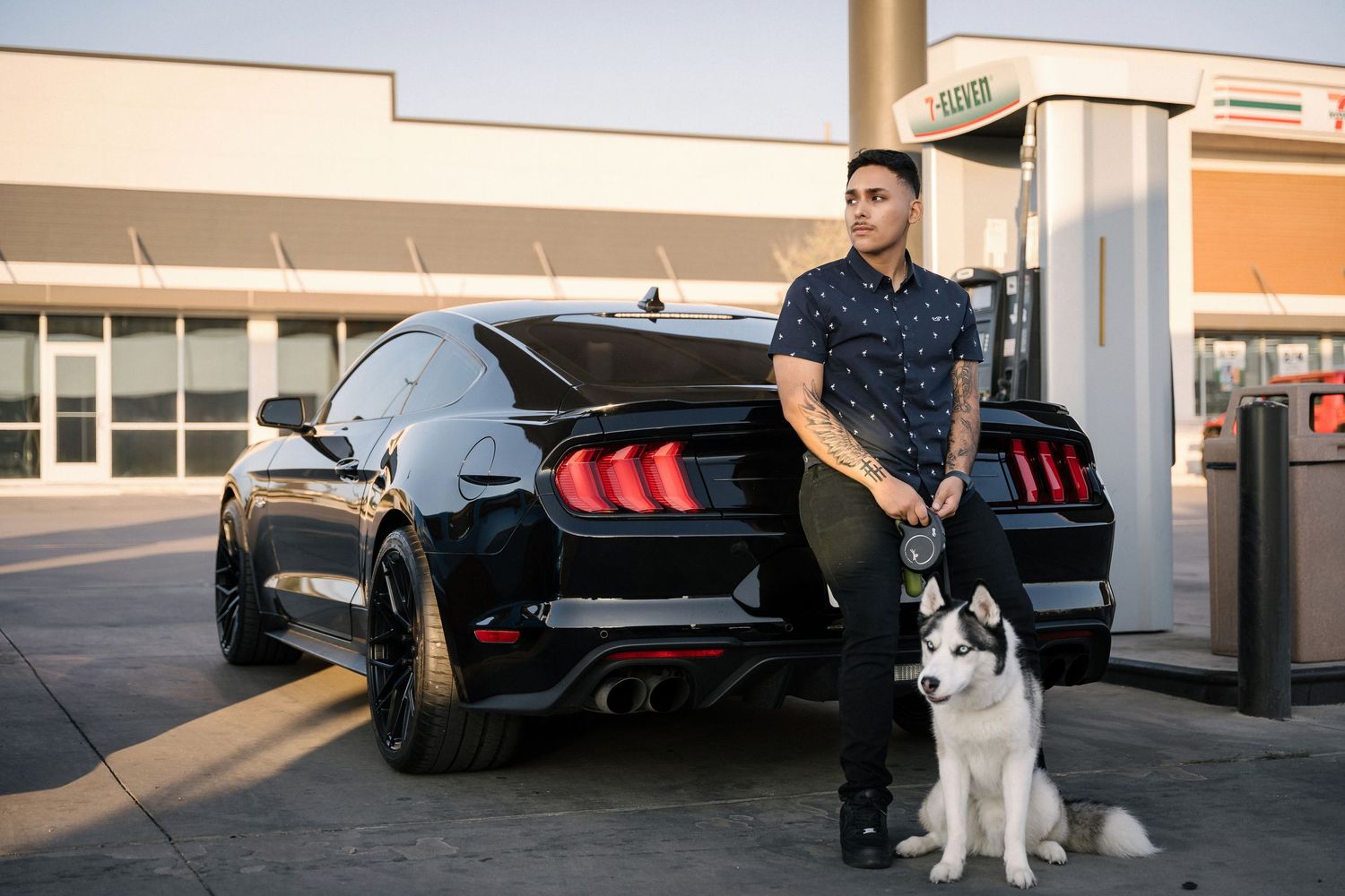 Person with white husky standing beside black Mustang with distinctive tail lights.