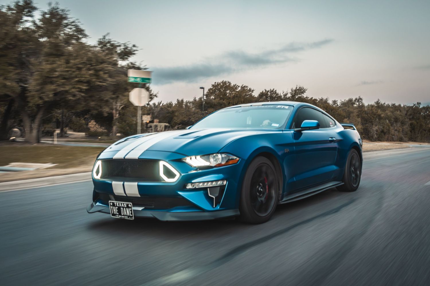 Modified blue Ford Mustang with LED headlights cruising on street.