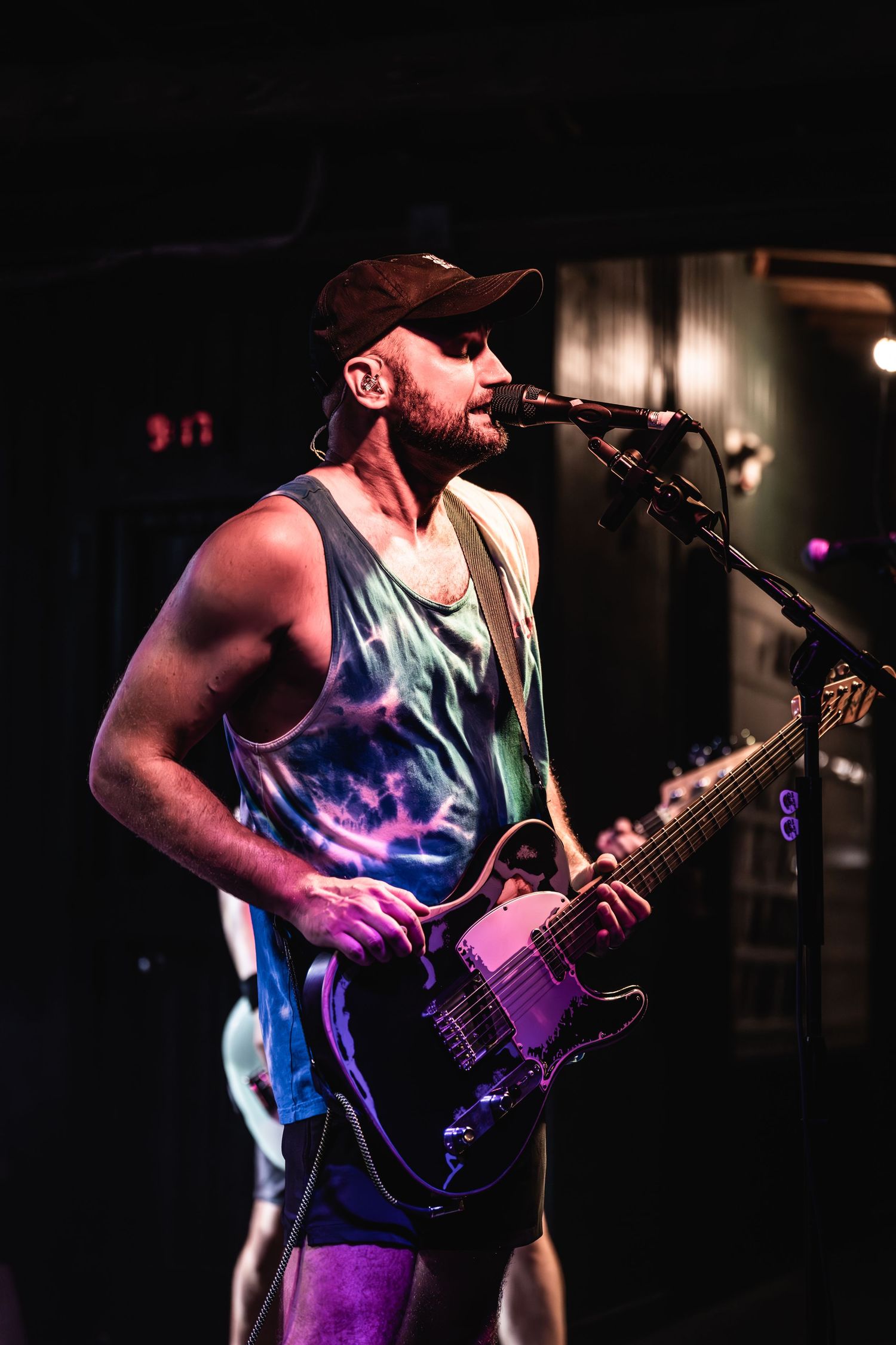 Musician plays guitar and sings into microphone during dimly lit concert performance.