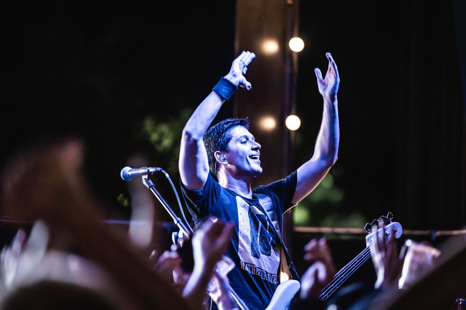 Concert performer raising hands under dramatic blue stage lighting during live show.