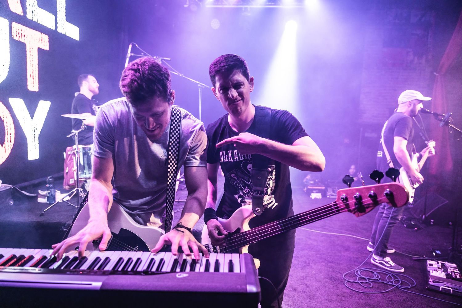 Two musicians collaborating on keyboard performance during energetic concert set.