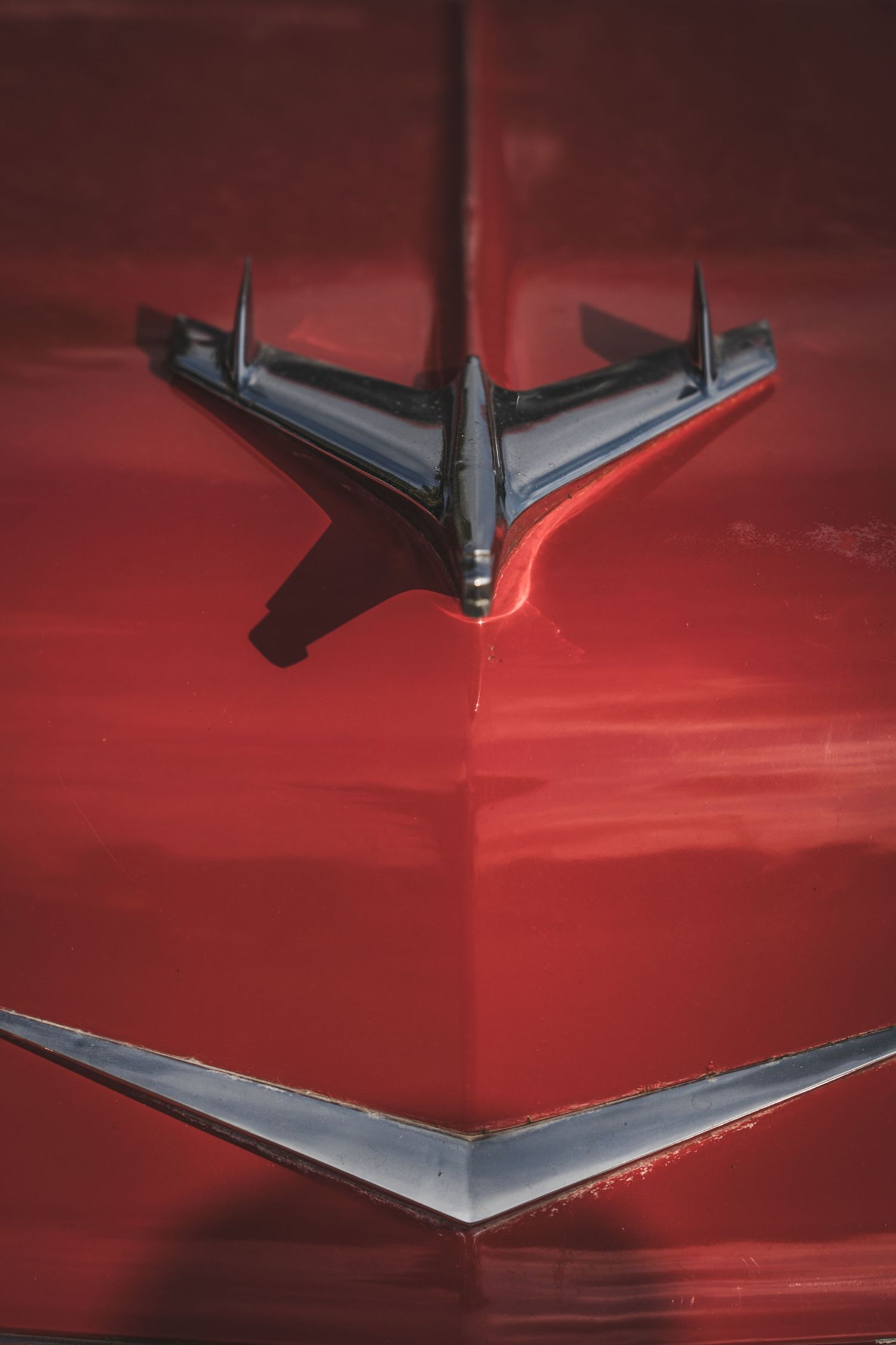 Vintage chrome hood ornament on a red classic car's bonnet.