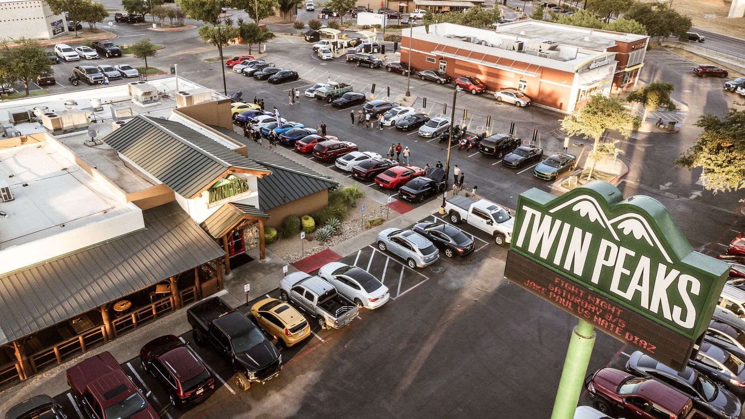 Aerial view of a shopping center parking lot with Twin Peaks restaurant signage visible at sunset.