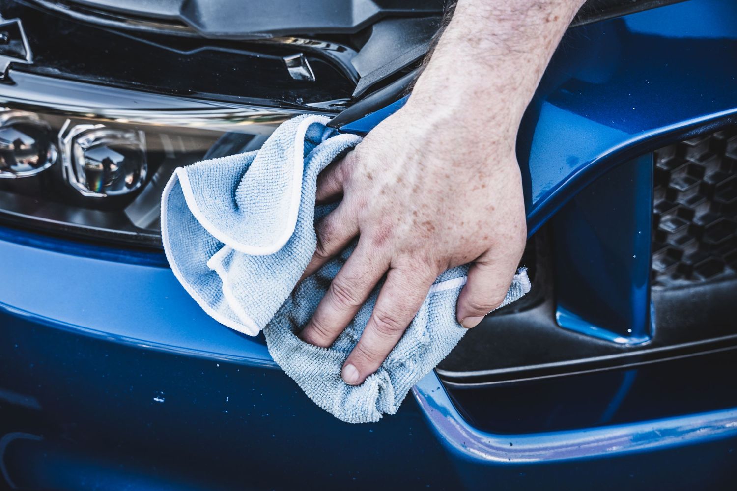 Hand wiping down a blue car exterior with a microfiber cloth during detailing.