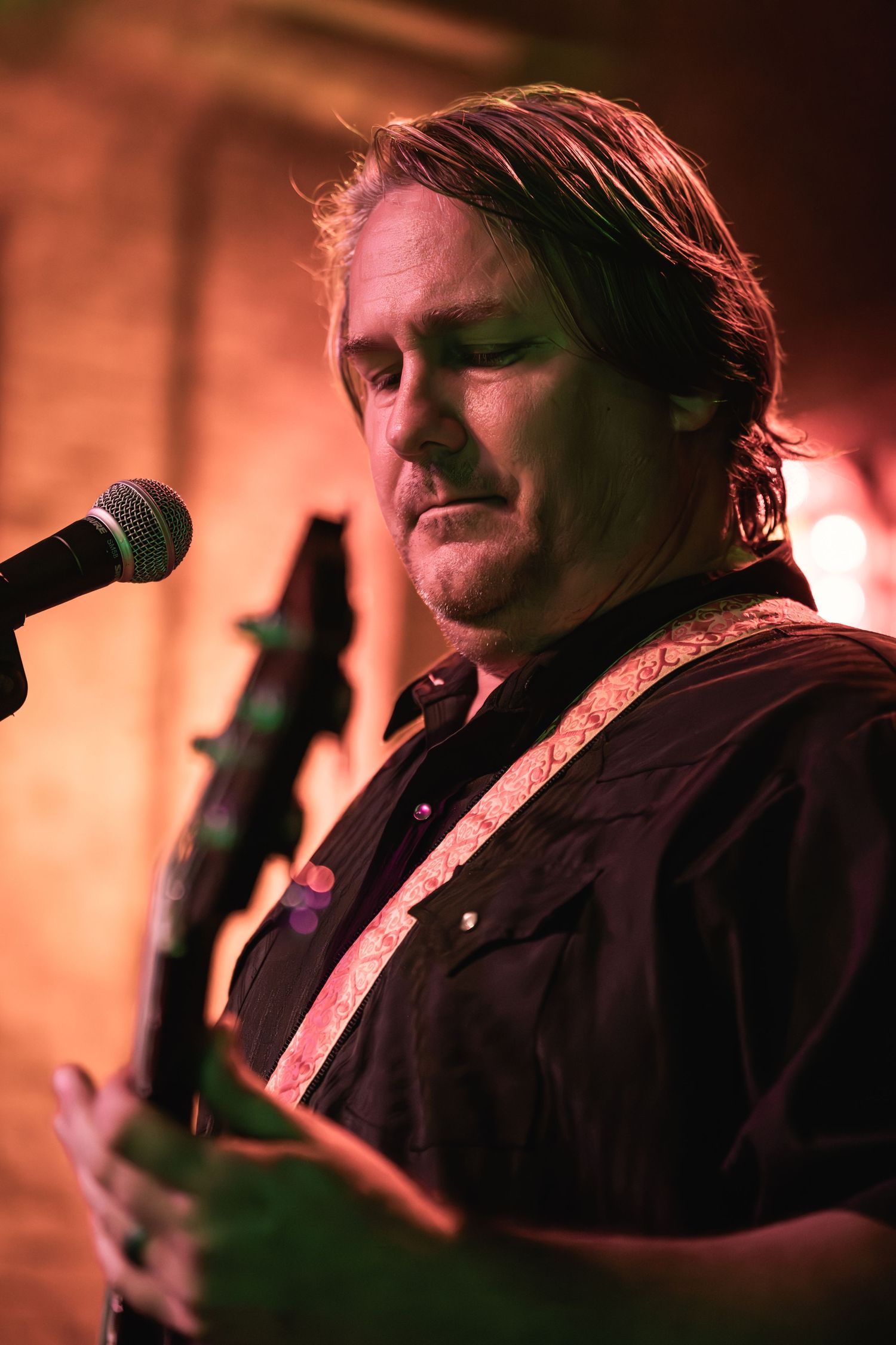 Musician singing into microphone with warm orange stage lighting backdrop.