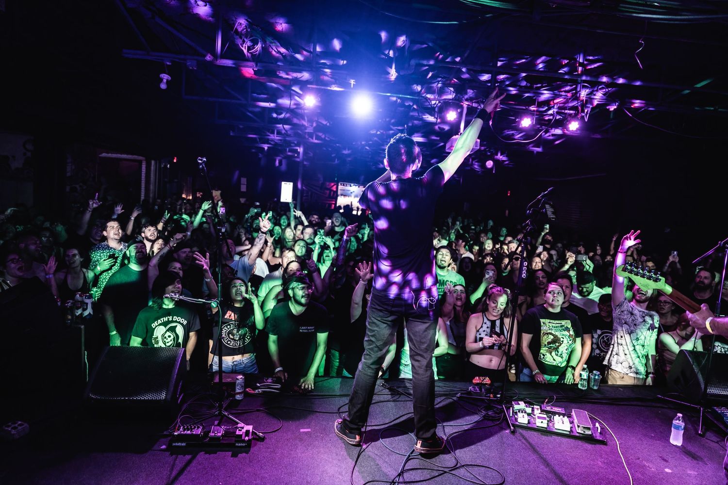 Concert crowd cheers as performer stands on stage with purple and green lighting overhead.