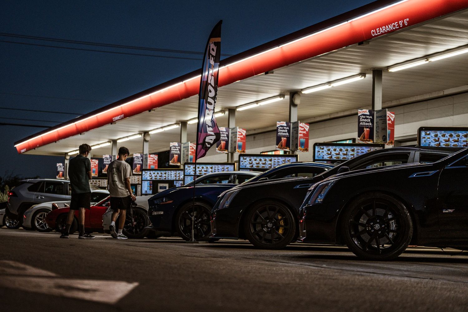 Performance vehicles lined up at a gas station during nighttime car meet.