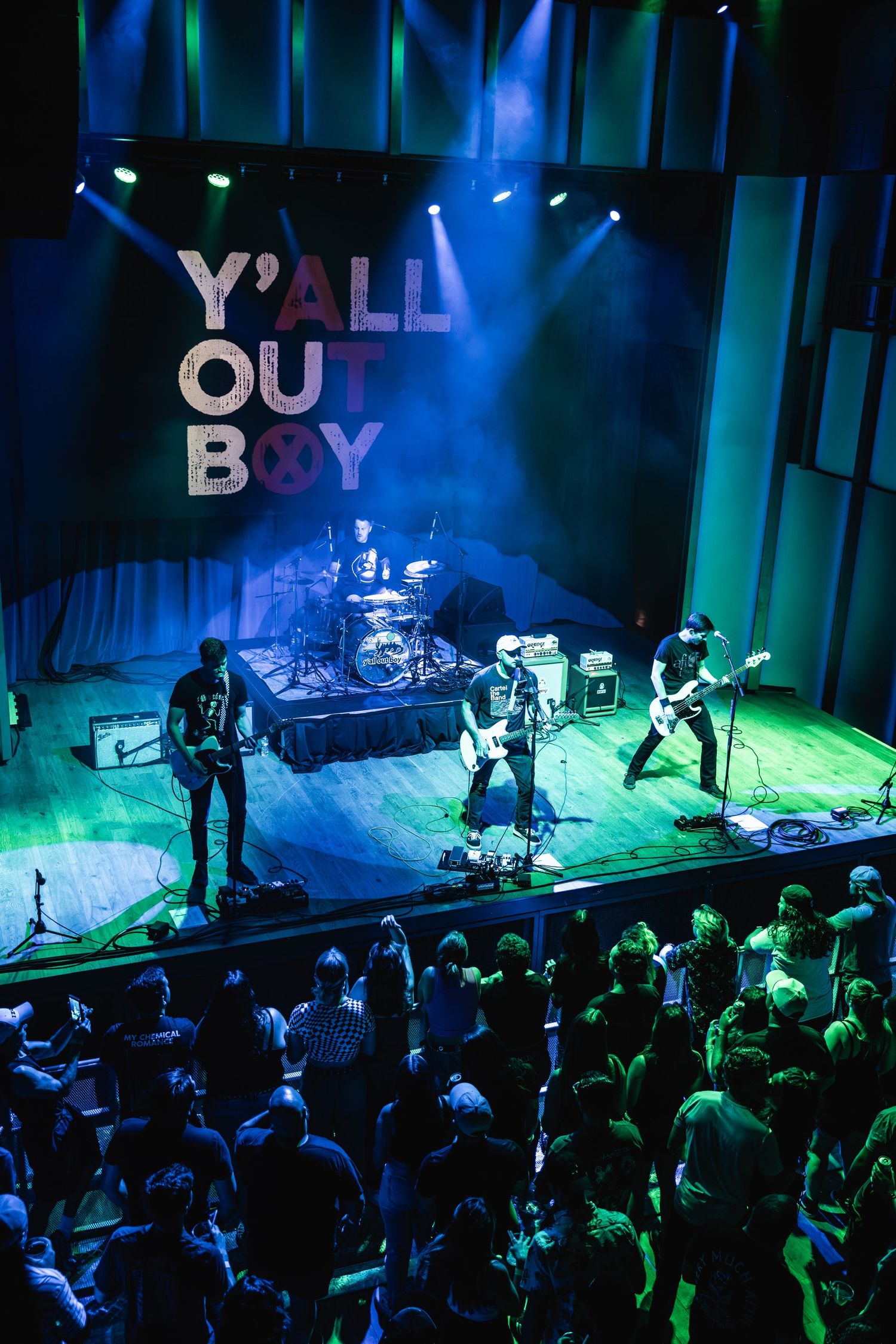 Band performs on elevated stage while crowd watches from below under atmospheric lighting.