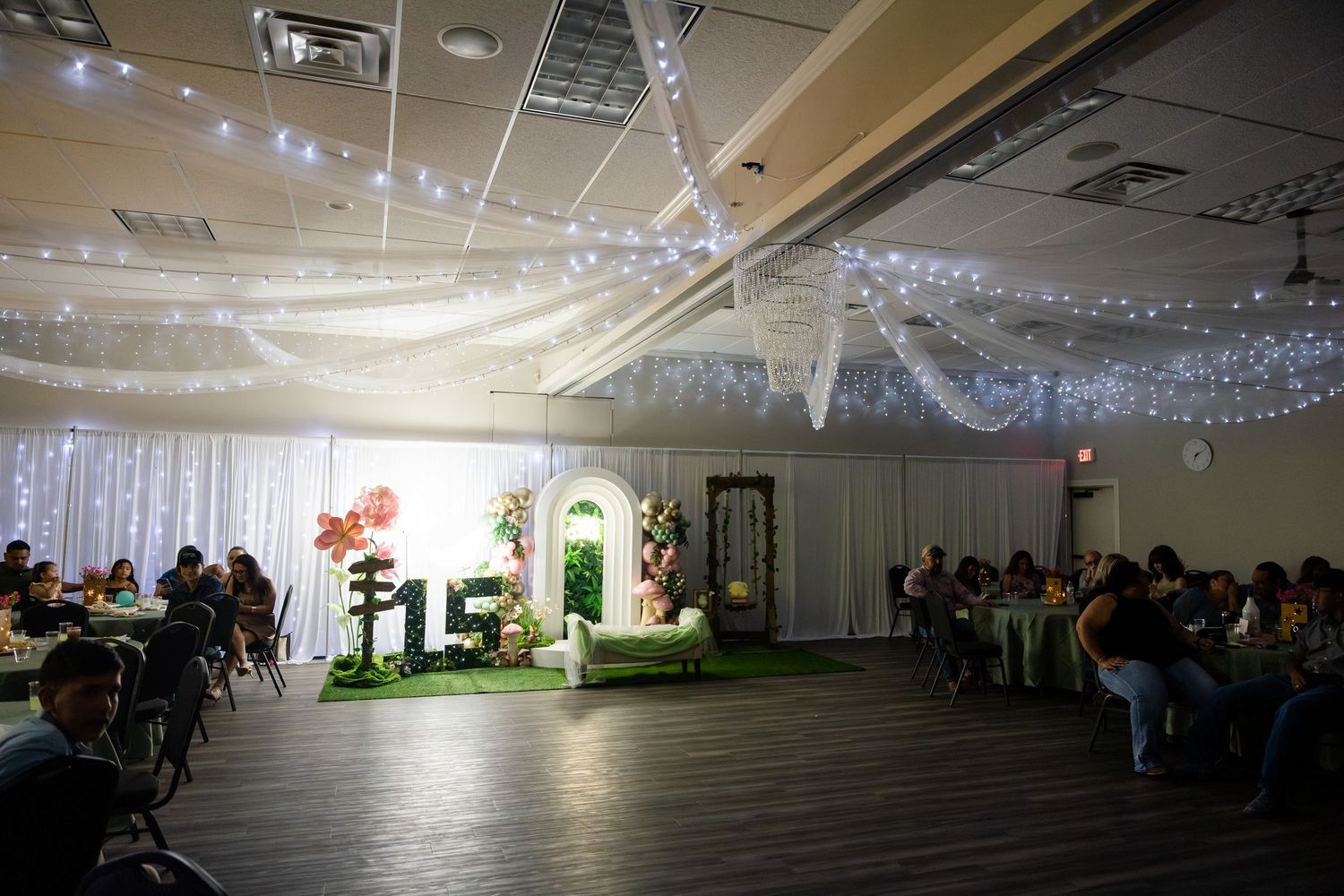 Elegant quinceañera venue with fairy lights, draped ceiling, floral arch, and 