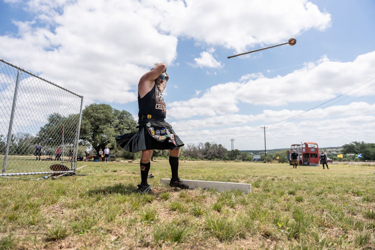 A man in a kilt competes in a Highland Games hammer throw event on a sunny day outdoors.