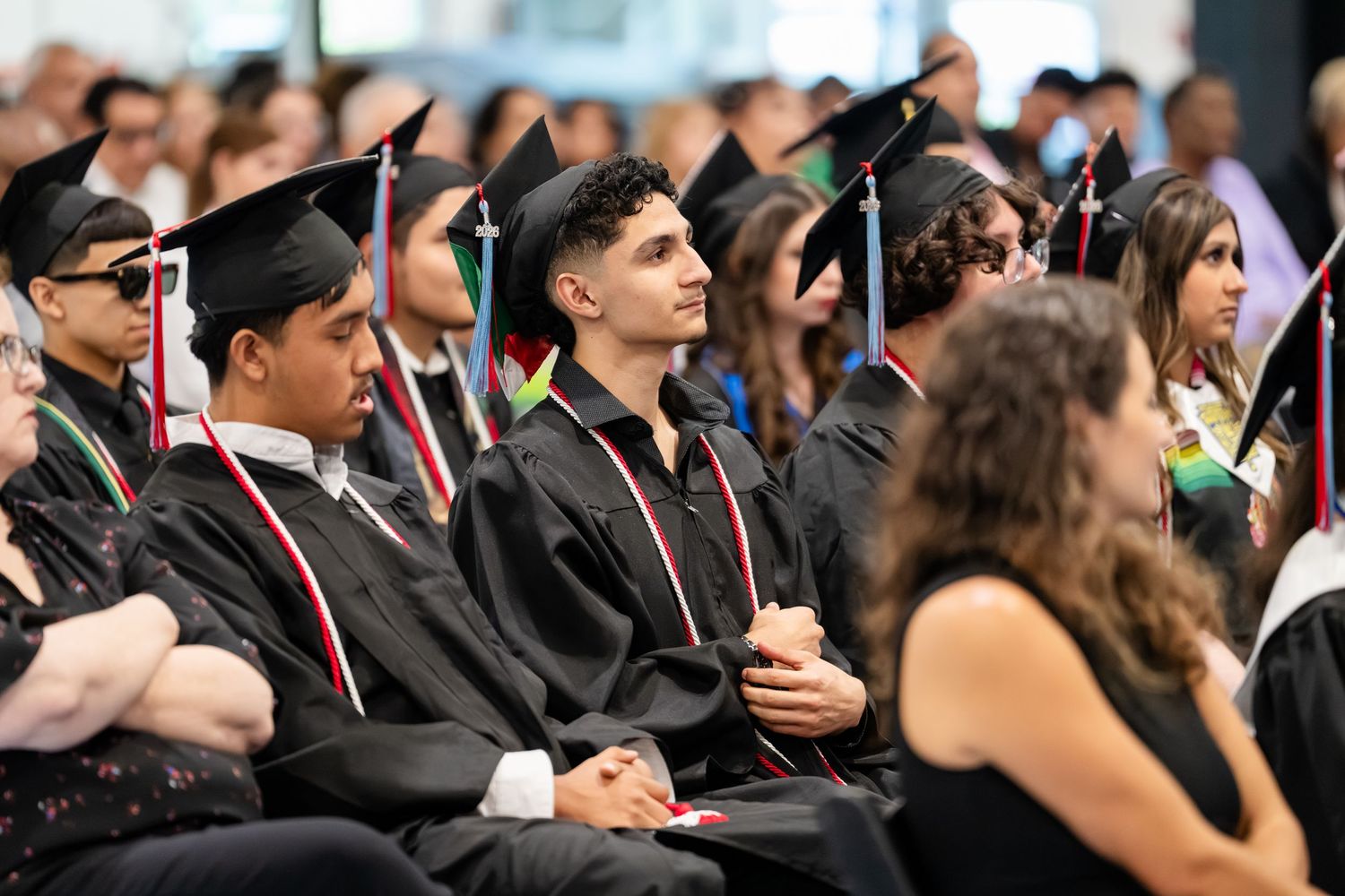 Students in black graduation caps and gowns seated at a commencement ceremony.