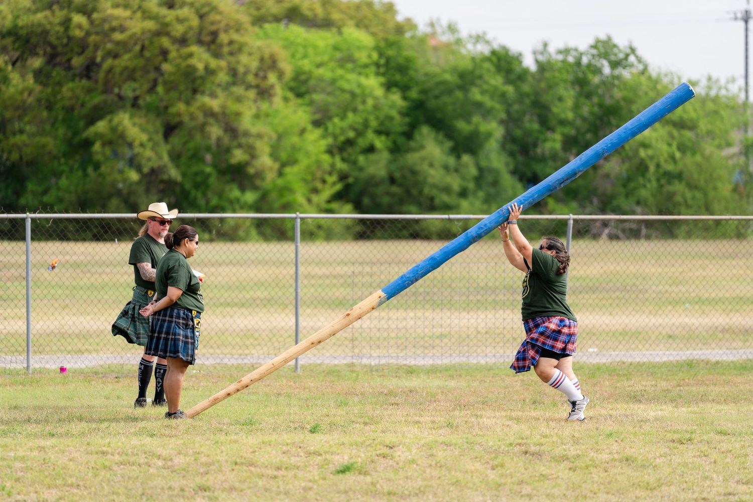 Athletes in kilts compete in caber toss at a Scottish Highland Games event on a grassy field.