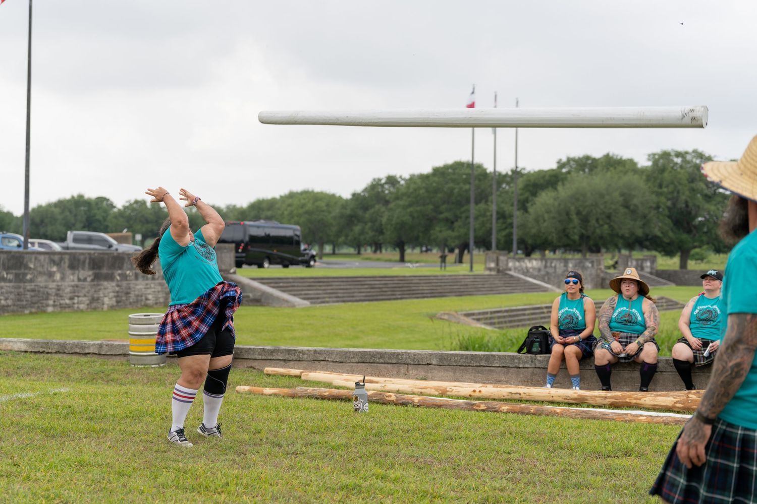 Athletes compete in Highland Games caber toss event on grassy field, spectators watching in traditional Scottish kilts.