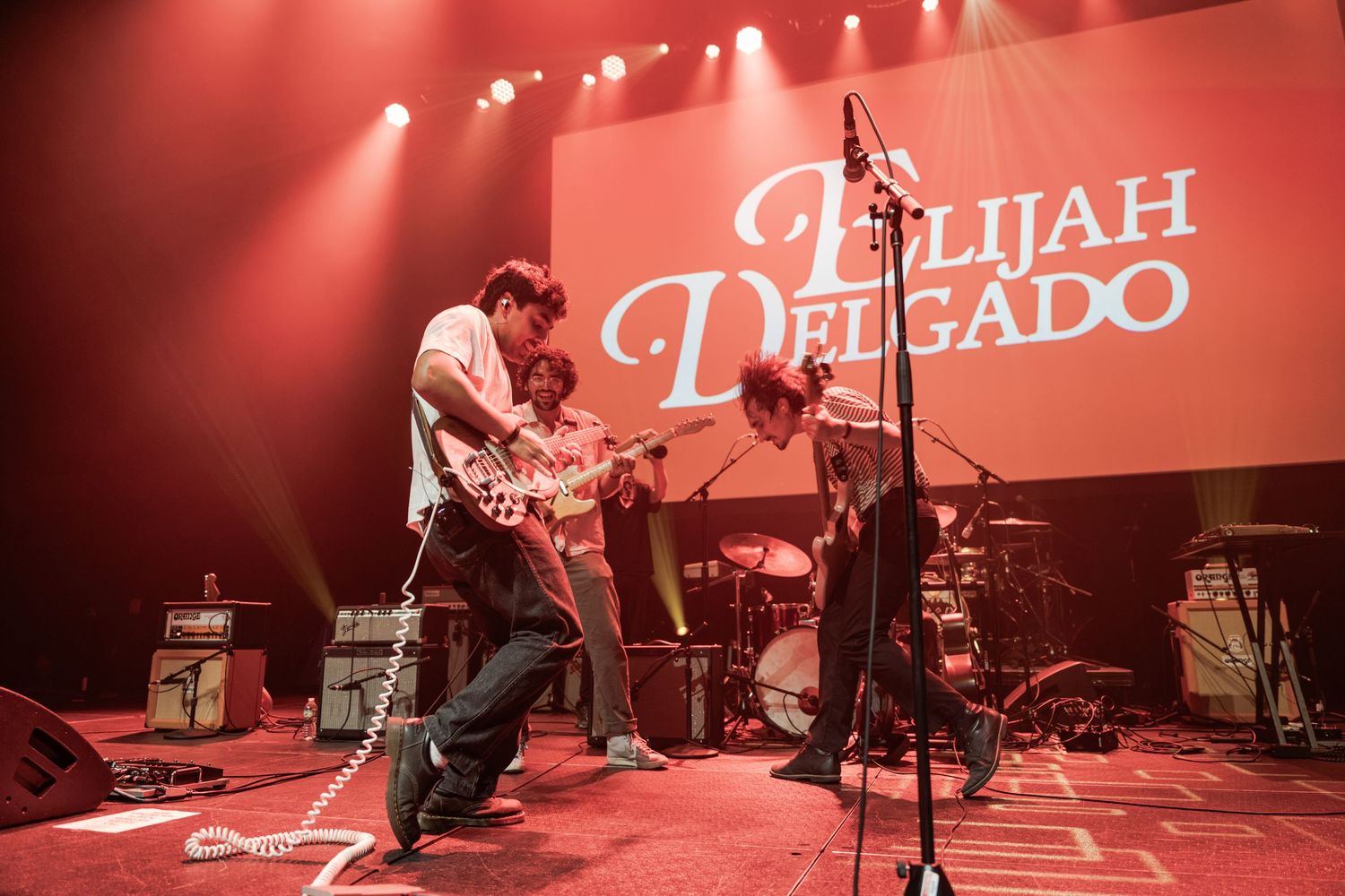Elijah Delgado band performing live on stage with guitars under red stage lights.
