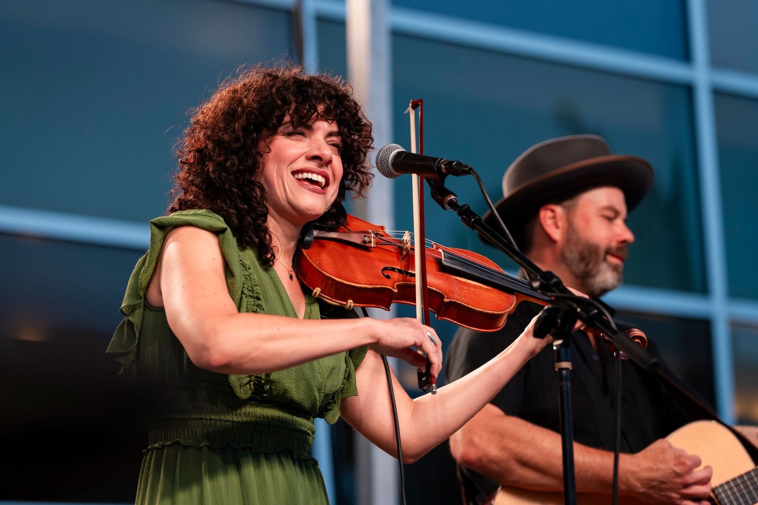 Musician in green dress plays violin on stage during live performance.