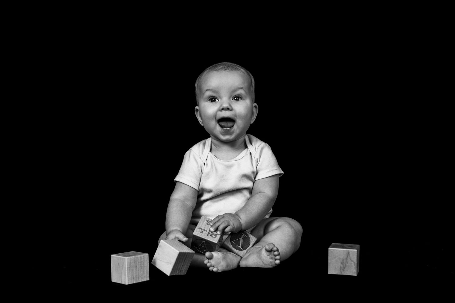 Black and white photo series showing a baby sitting and playing with wooden blocks on a dark background.