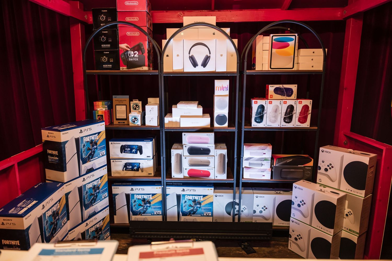A panoramic view of a modern electronics store display with headphones and audio equipment arranged on shelves with red lighting.