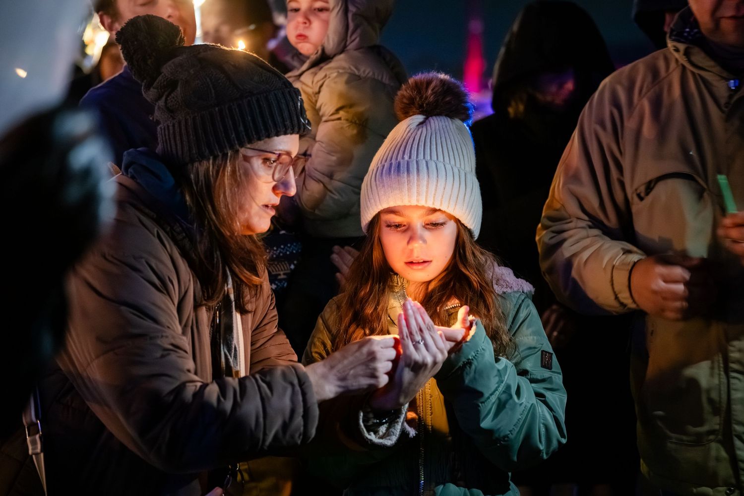 A group of people hold candles during a candlelight vigil ceremony in a dark room.
