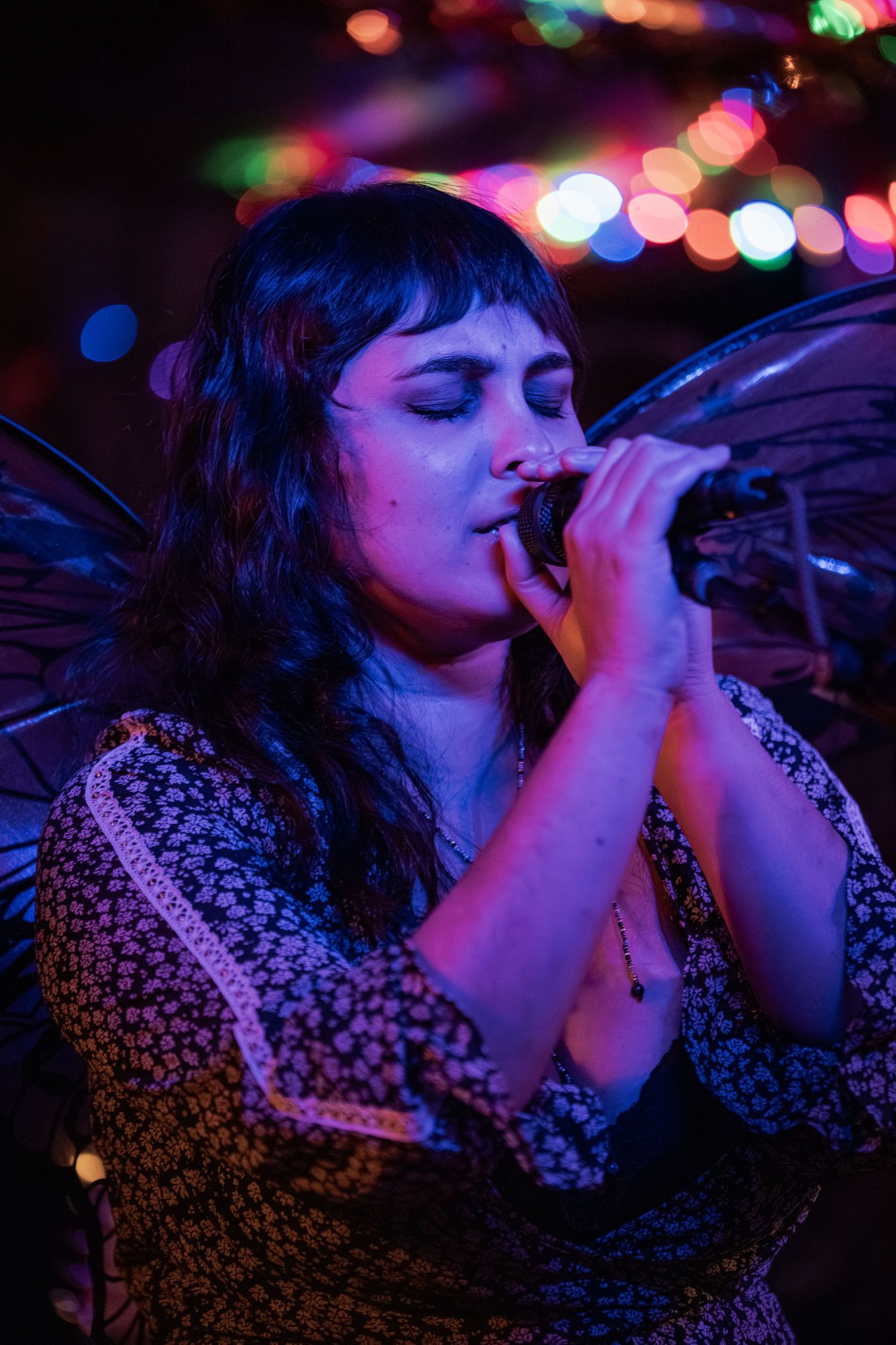 A performer sings passionately on stage with colorful bokeh lights in the background creating a dreamy atmosphere.