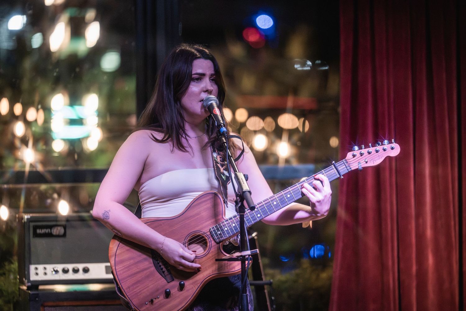 A musician performs on stage with a guitar under purple and blue lighting at a live music venue.