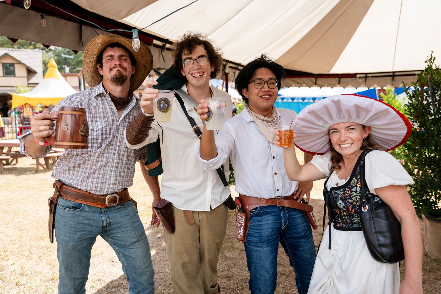 Four friends celebrating at an outdoor festival with beer steins and traditional Bavarian attire.