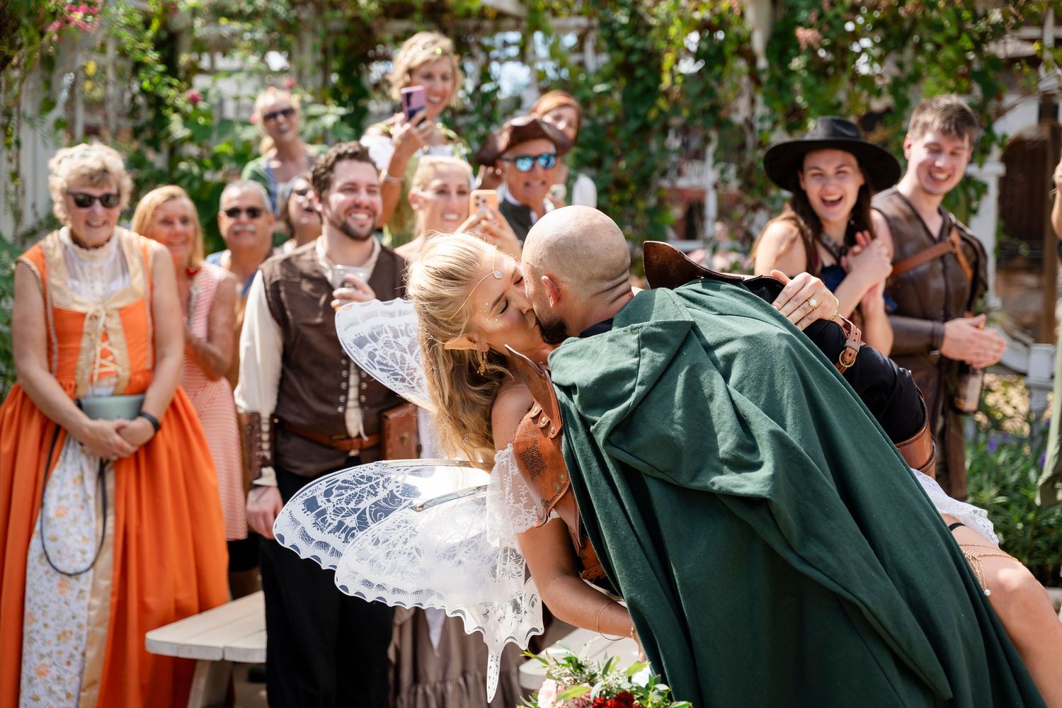 Wedding party celebrates with joyful reactions during outdoor ceremony in orange and green attire.