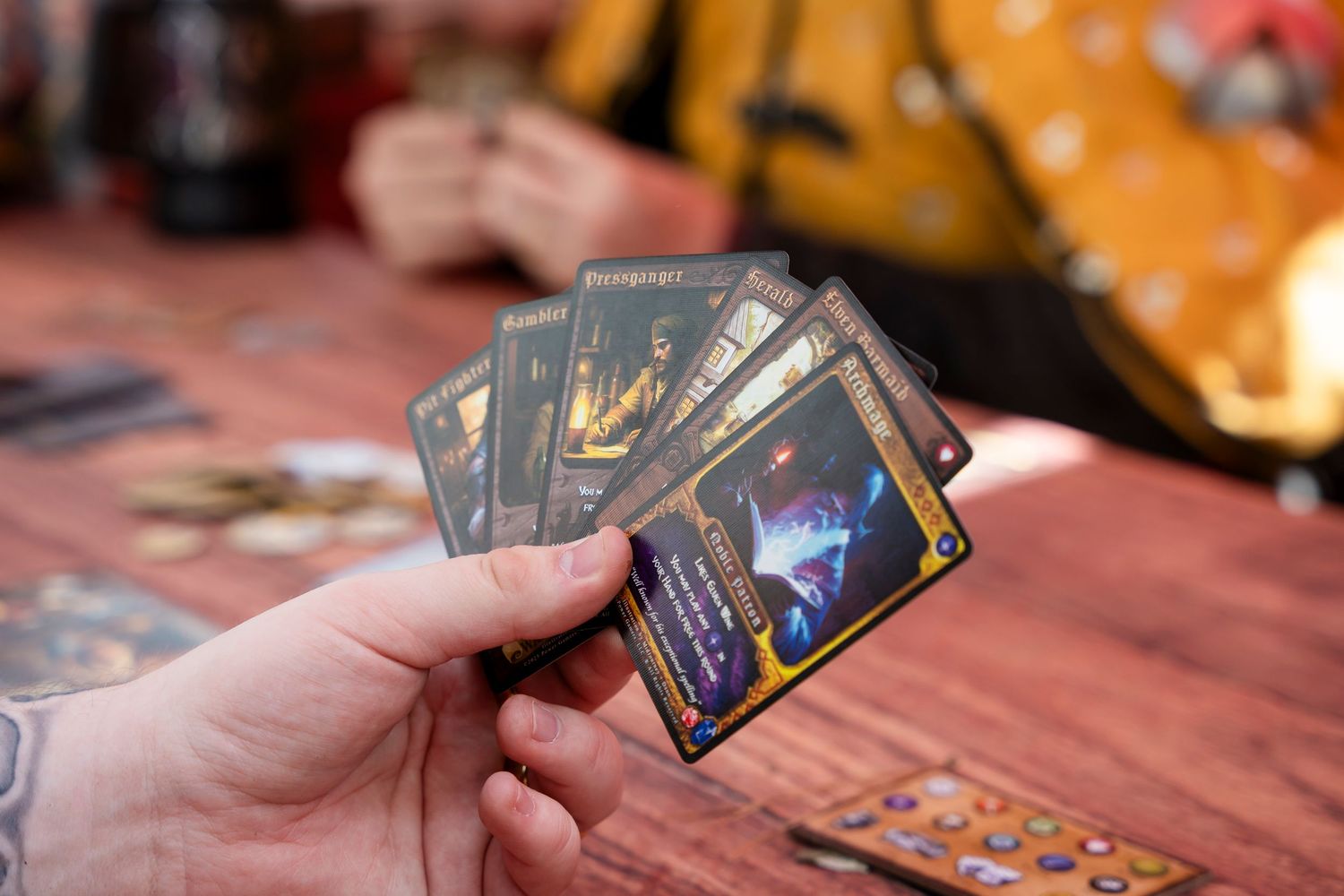 Multiple hands holding playing cards around a wooden table during a card game.