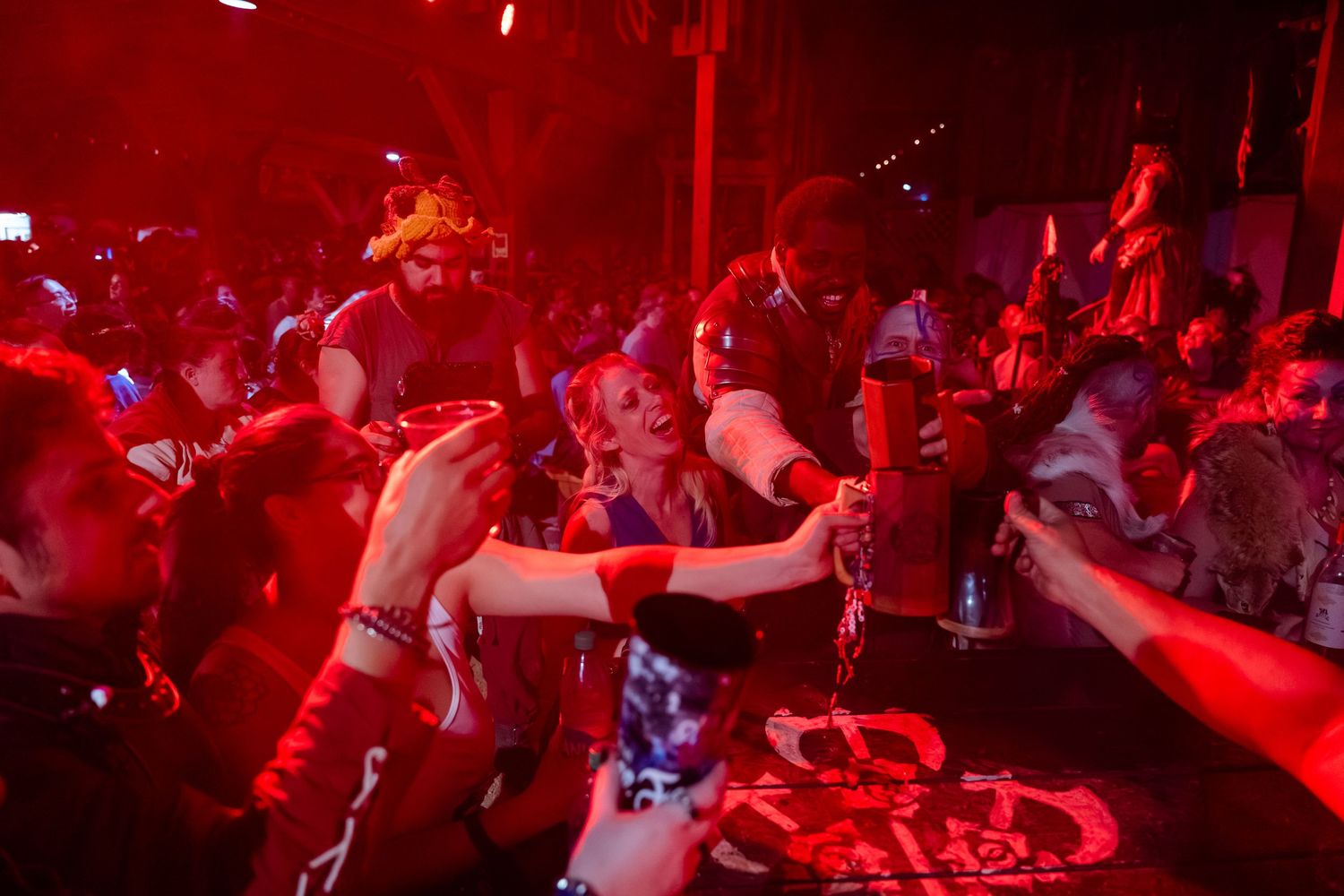 Crowd of people dancing and celebrating in a nightclub bathed in vibrant red lighting.