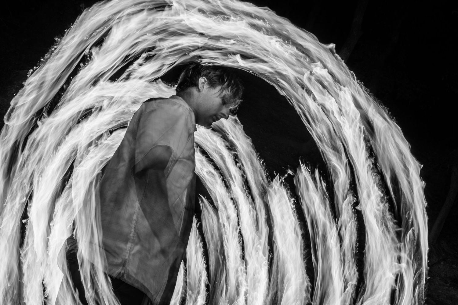 Black and white photo showing a figure surrounded by a dramatic circular light trail created through long exposure.