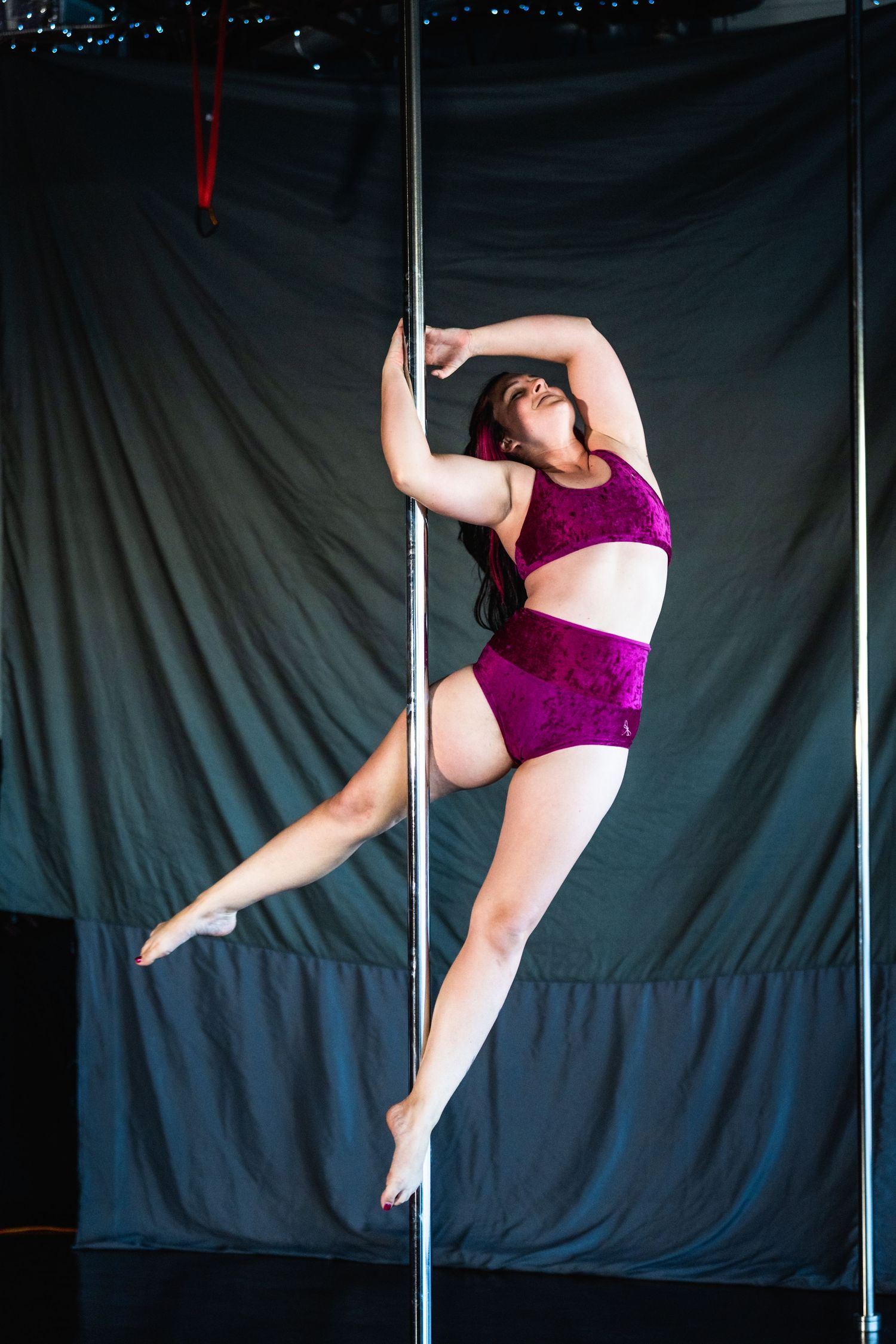 A pole dancer in purple attire performs a dynamic spinning sequence against a dark backdrop.