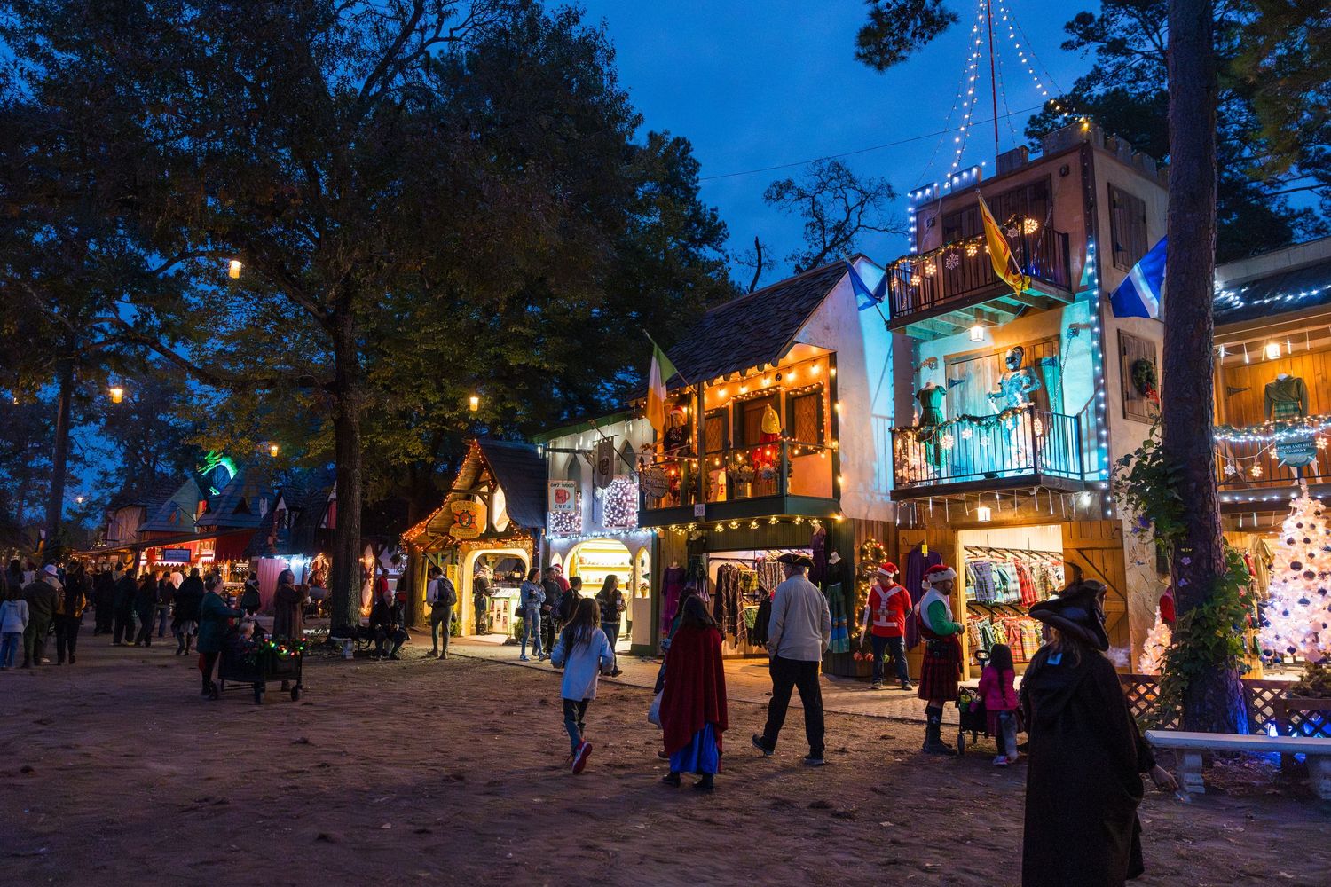 Illuminated storefronts and holiday lights create a festive evening atmosphere along a charming shopping street.