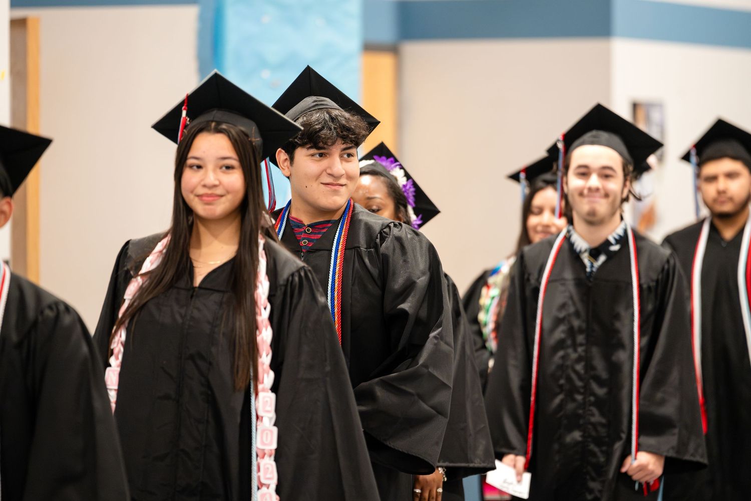 Graduates wearing traditional black caps and gowns walking in line during a commencement ceremony.