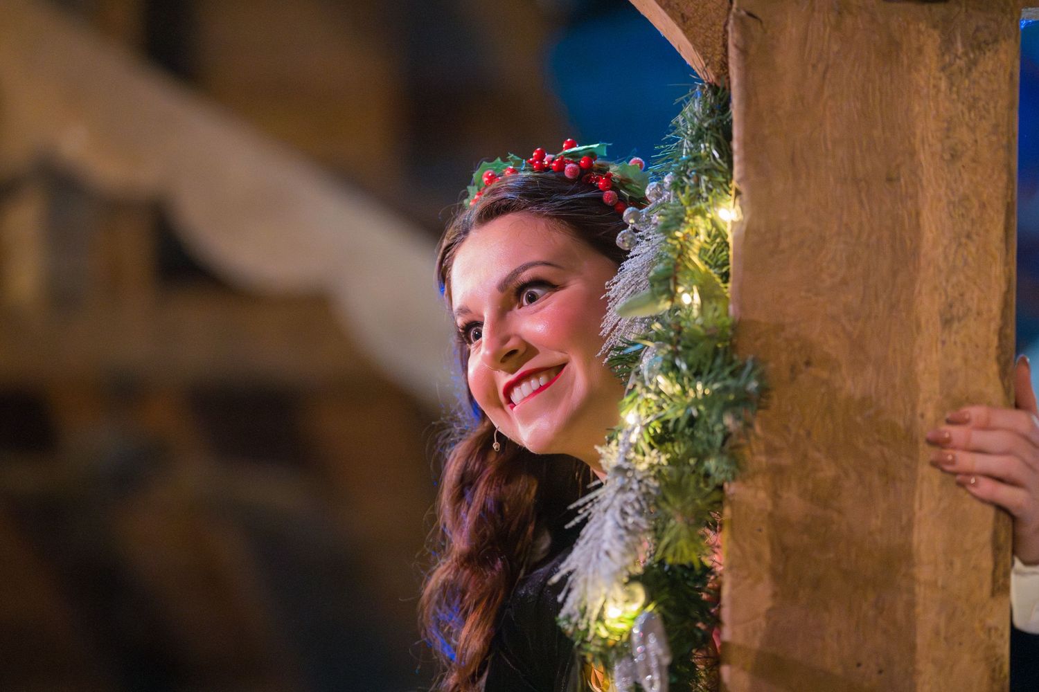 A wedding party poses in a rustic barn setting with warm lighting and decorative greenery overhead.