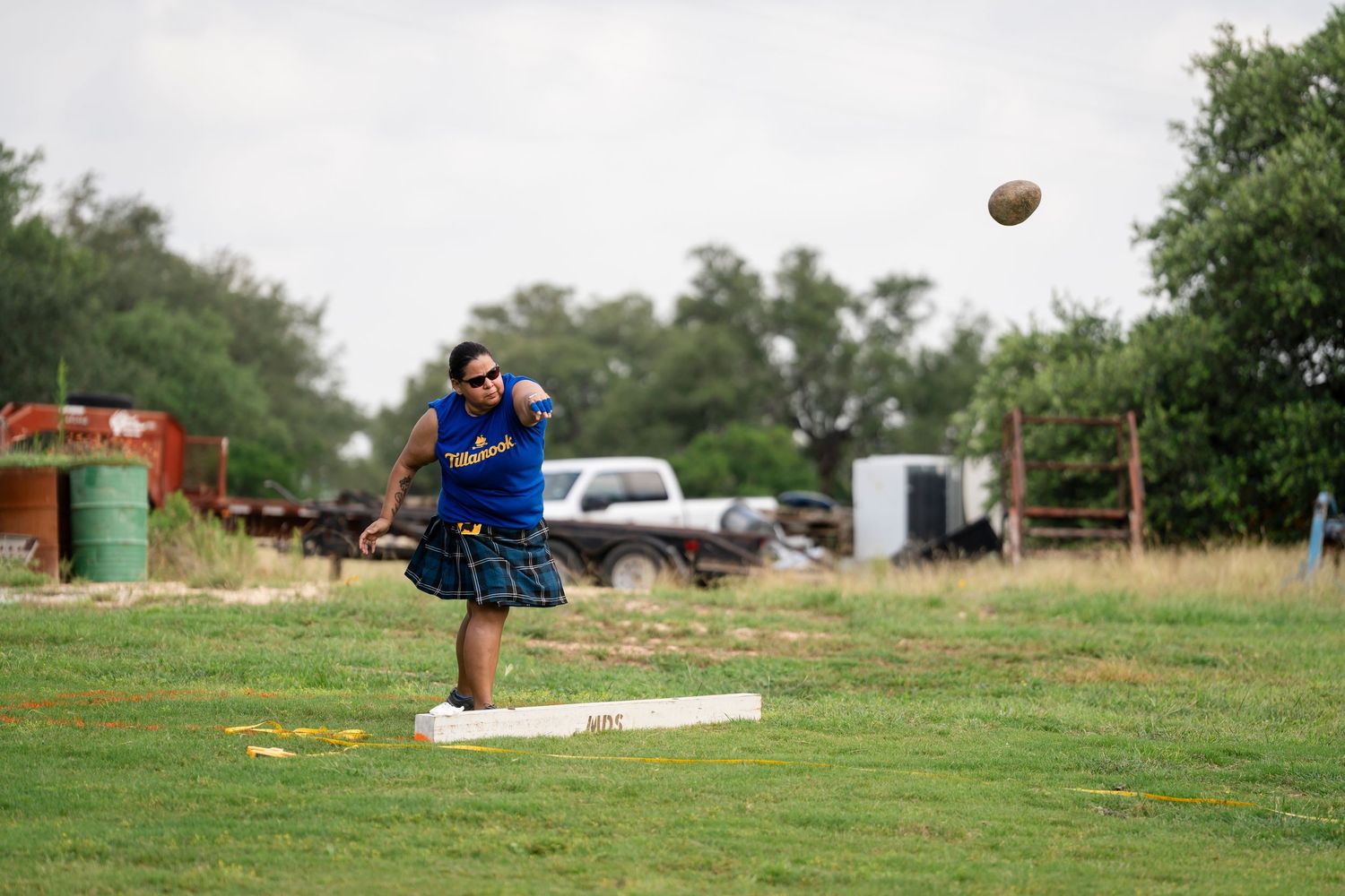 A football spirals through the air over a green grass field on a cloudy day.