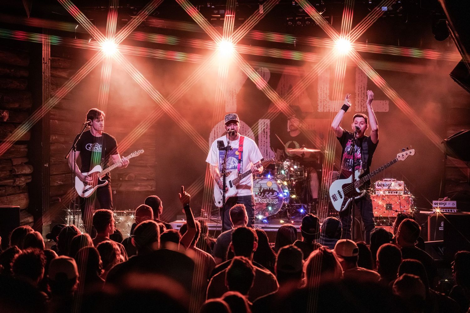 Rock band performs on stage with dramatic red lighting while crowd watches at an energetic live concert.