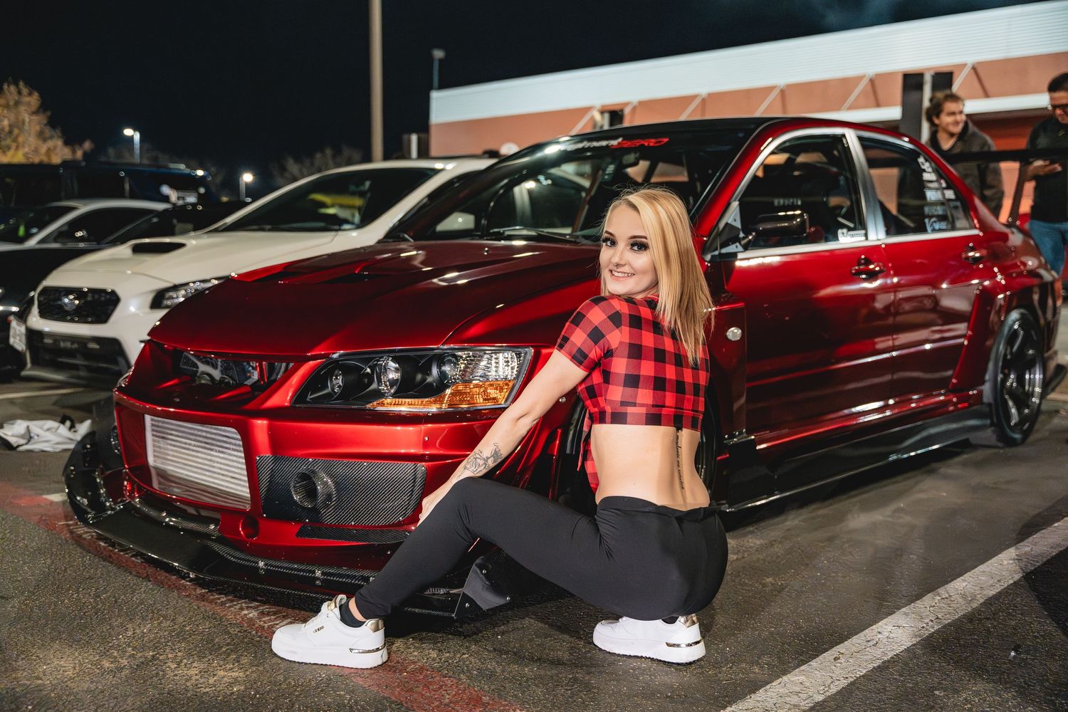Modified red Mitsubishi Evolution posed with matching red plaid fashion theme at night.