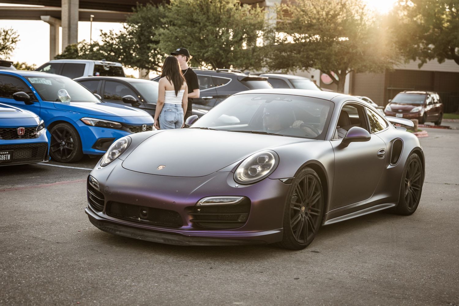 Sleek gray Porsche 911 Turbo parked at sunset during a car show.