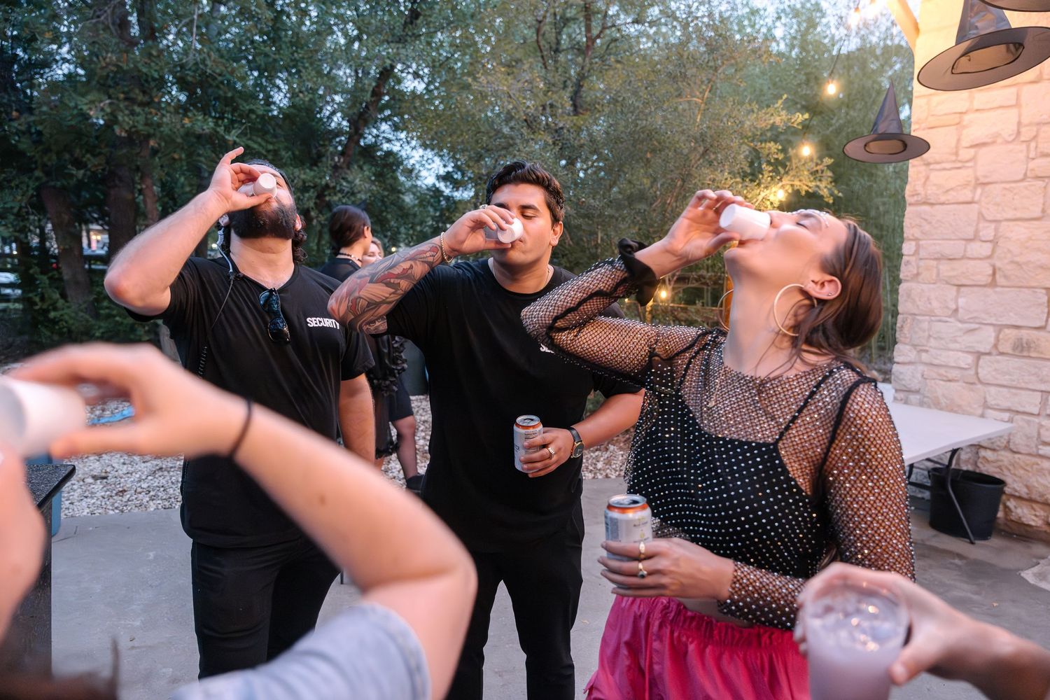 A group taking shots at an outdoor party with string lights and trees in the background.