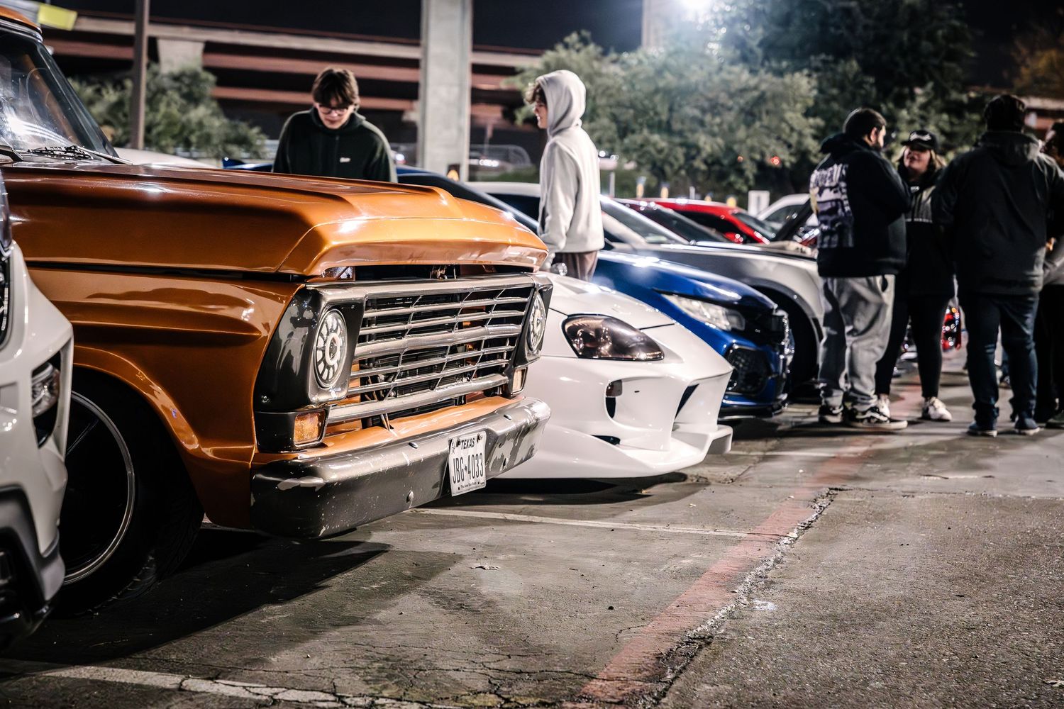 Classic orange truck parked alongside modern sports cars at an automotive gathering.